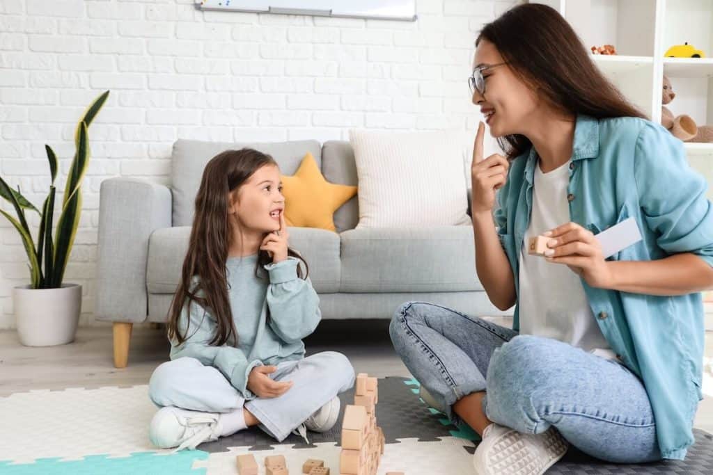 Female speech therapist teaching little girl how to pronounce letters